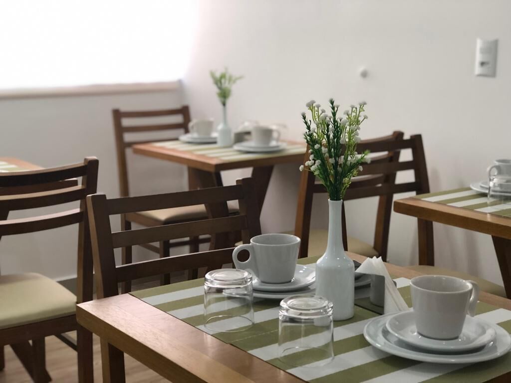 A dining area with wooden tables and chairs, white tableware, and a vase with flowers.