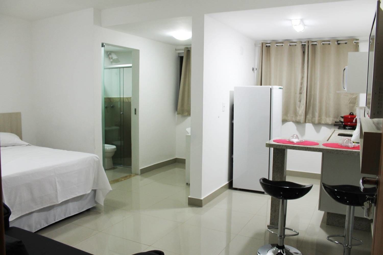 Habitación de hotel con cama, ducha, inodoro, lavamanos y una pequeña cocina con refrigerador y microondas.