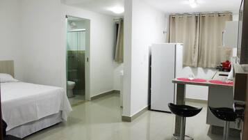 Habitación de hotel con cama, ducha, inodoro, lavamanos y una pequeña cocina con refrigerador y microondas.