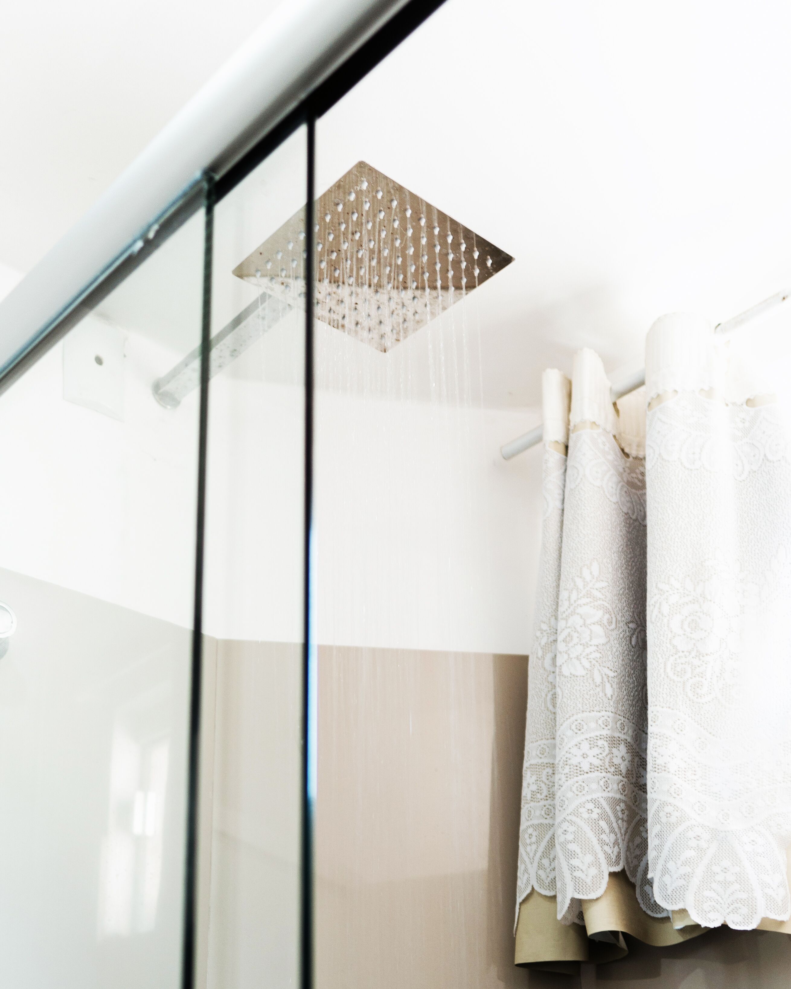 A shower with a square, perforated ceiling and a glass door.
