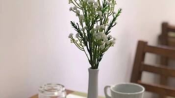 Een eettafel met witte kopjes en schoteltjes, een witte vaas met witte bloemen, en een geruit placemat.