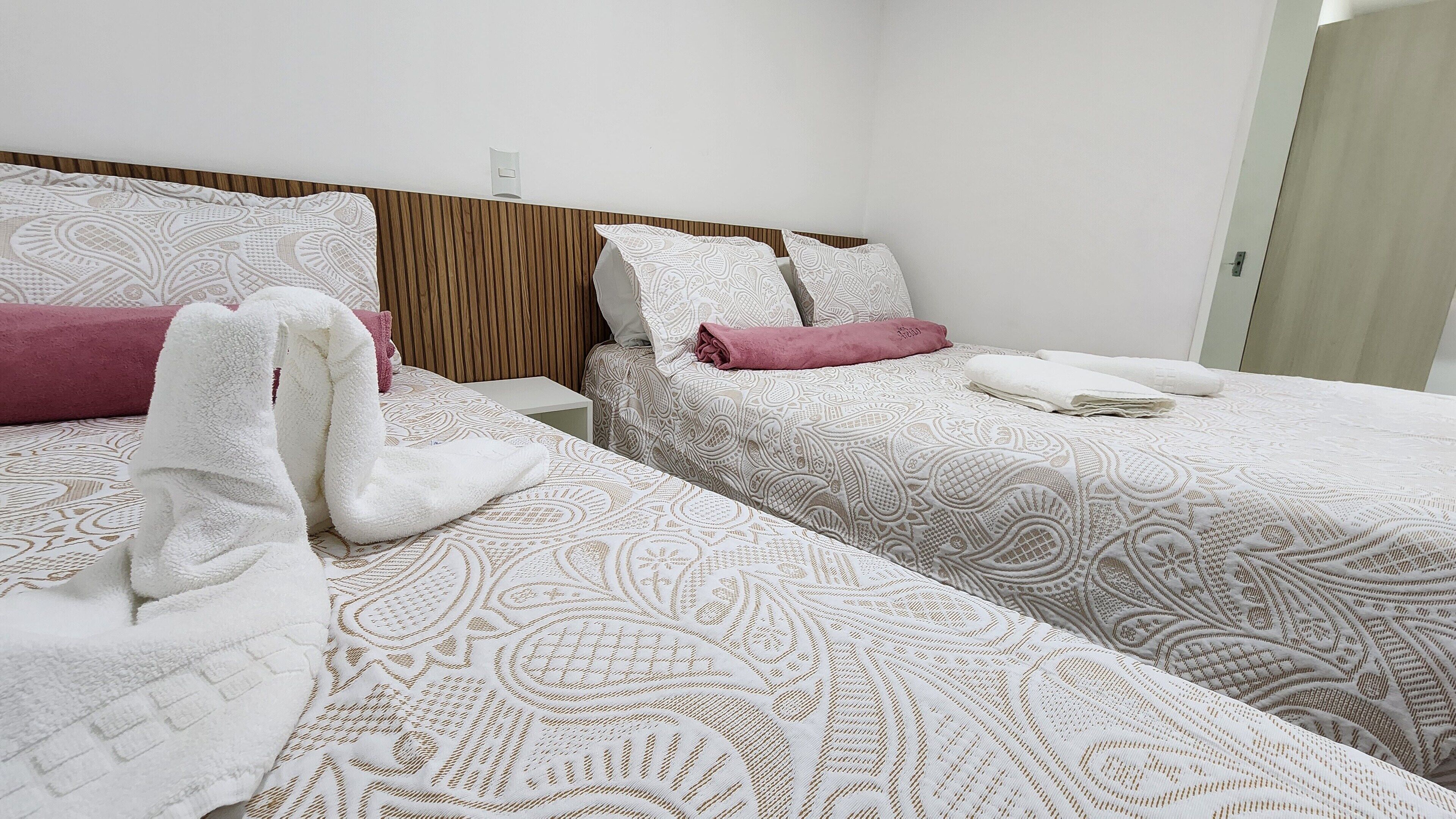 Une chambre d’hôtel avec deux lits, chacun agrémenté de draps à motifs et d’un oreiller rose.