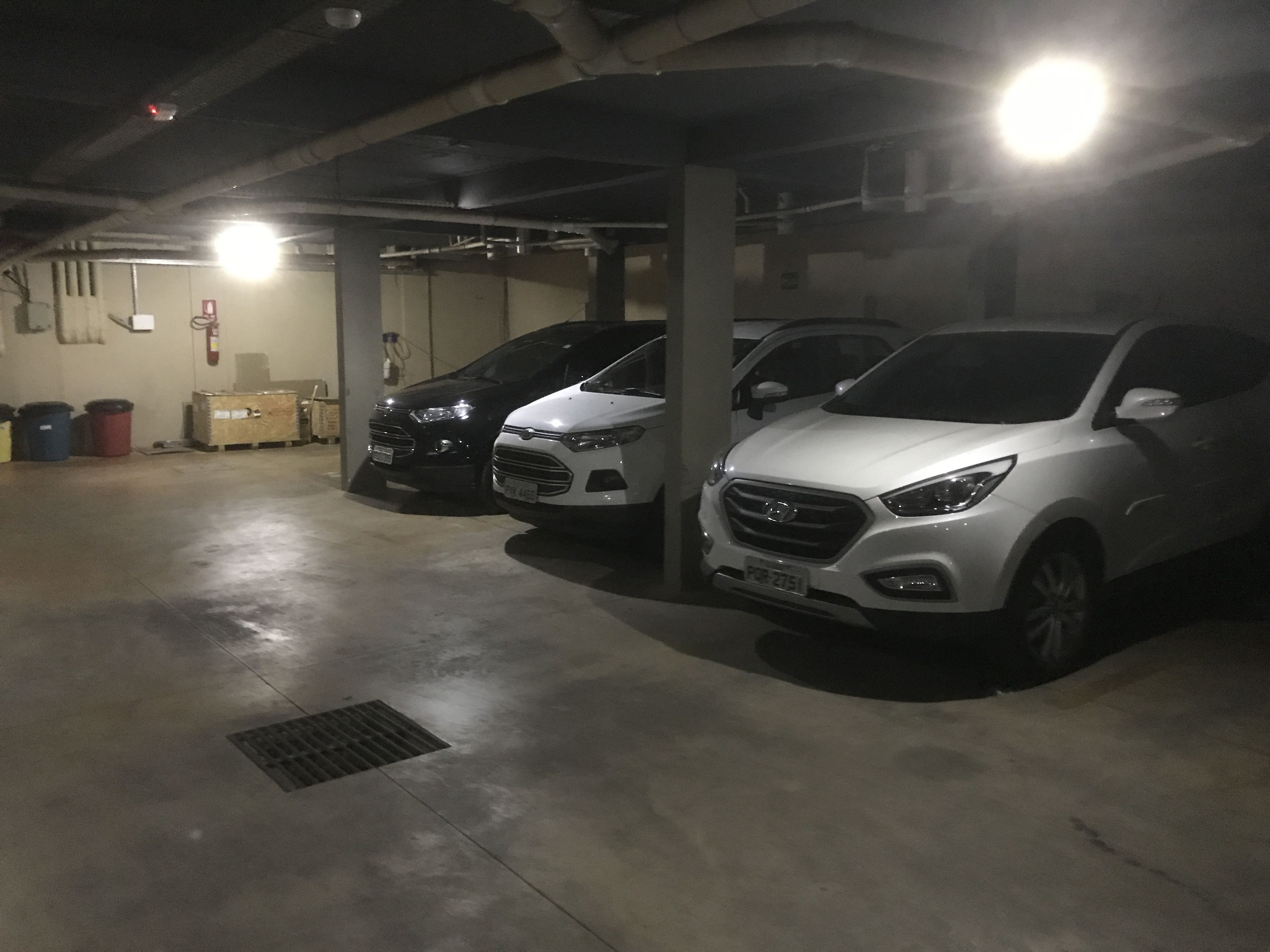 Un aparcamiento con tres coches aparcados en fila, suelos de hormigón y tuberías del techo visibles.