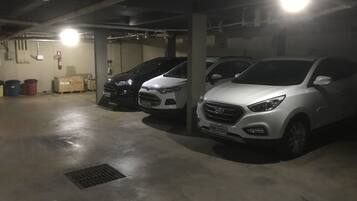 Eine Parkgarage mit drei in einer Reihe geparkten Autos, Betonböden und sichtbaren Rohren an der Decke.