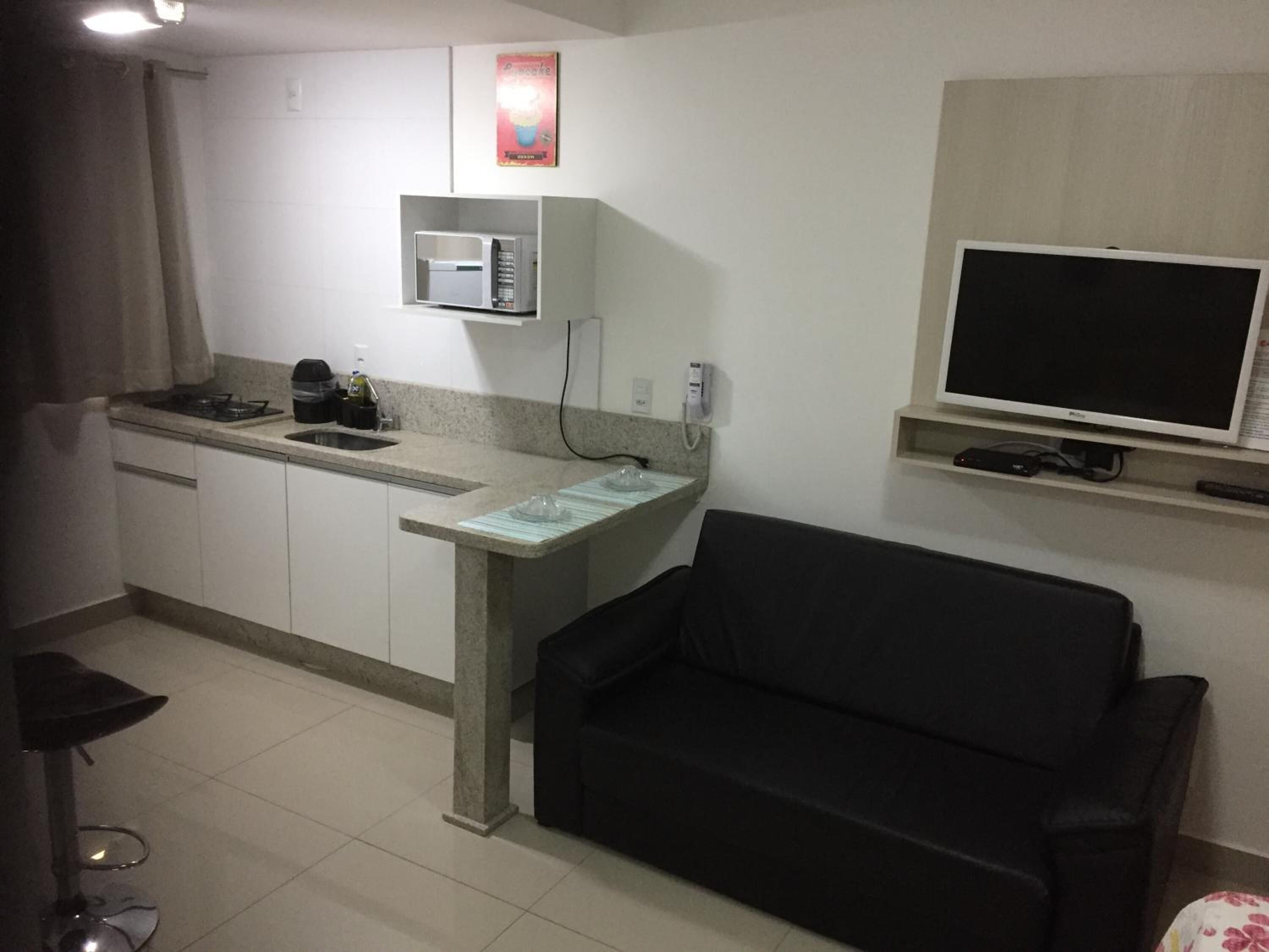 A compact living space with a kitchenette, a black sofa, a flat-screen TV, and a microwave.