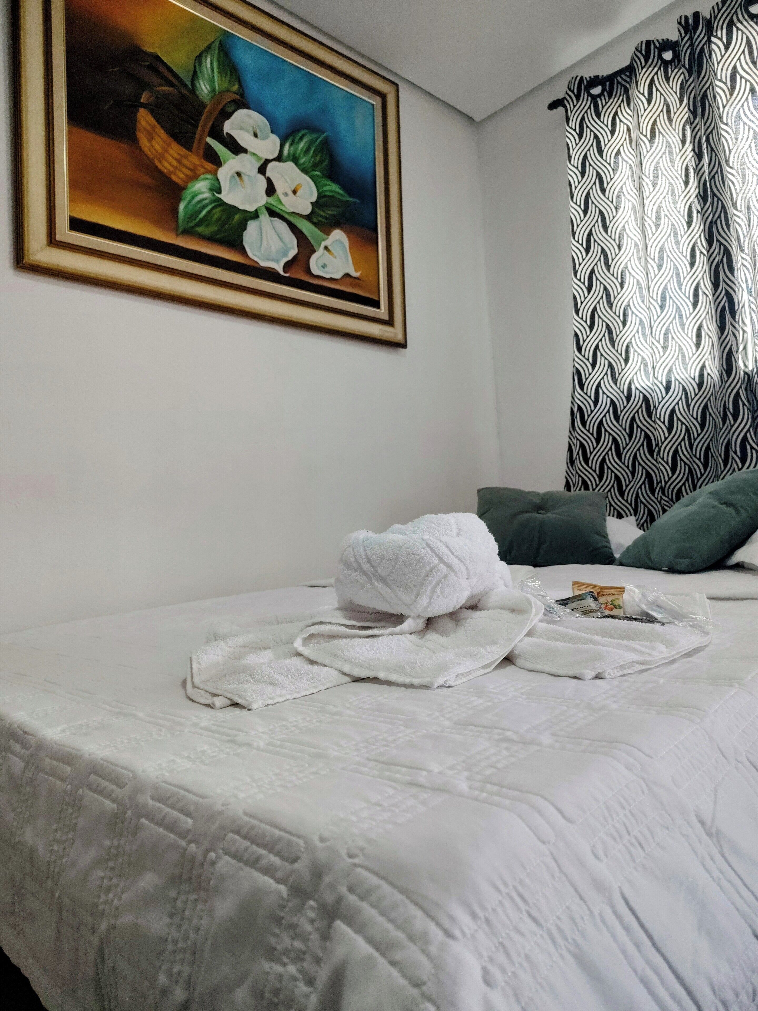 A hotel room with a bed, a painting on the wall, and a patterned curtain.