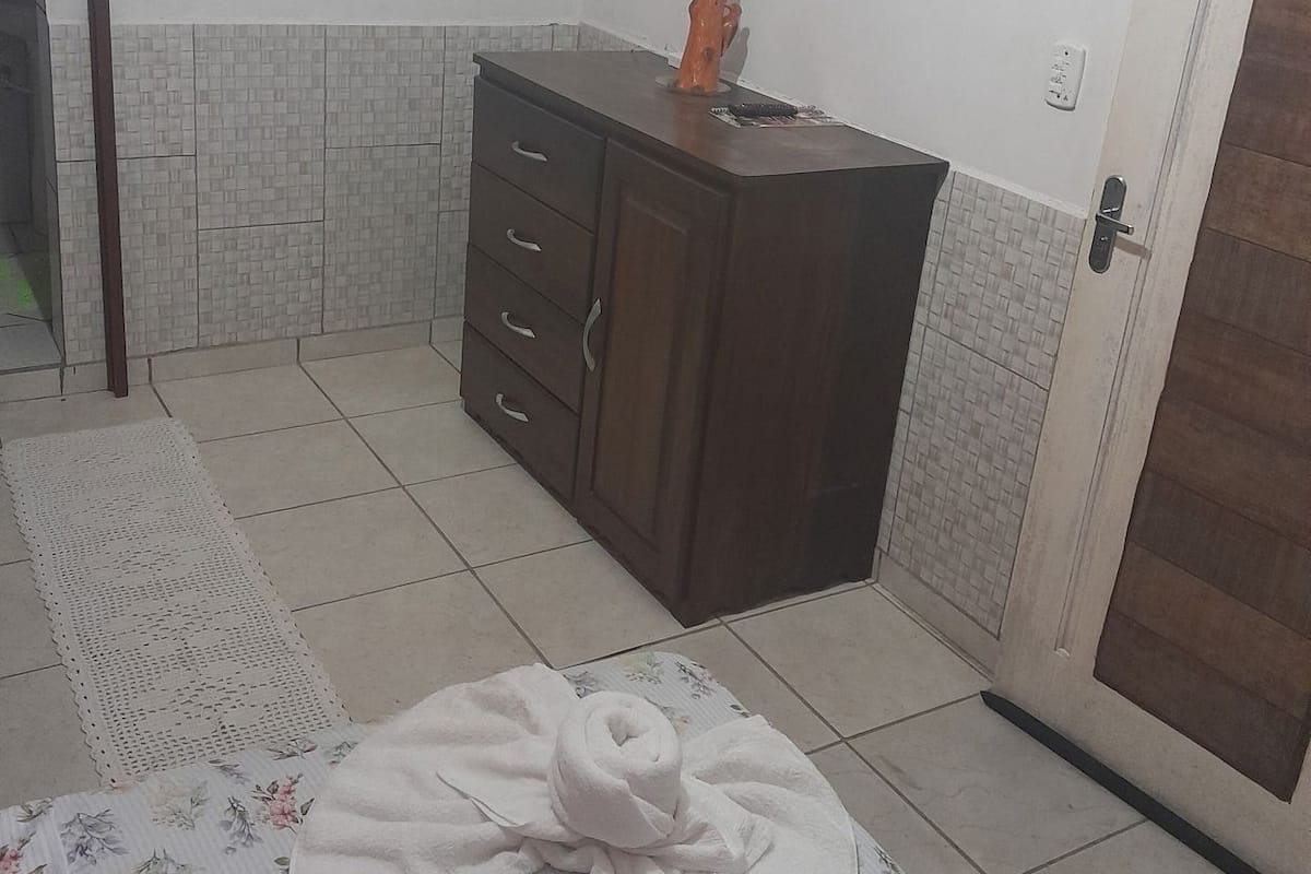 Quarto com cama, cômoda, televisão na parede e porta.