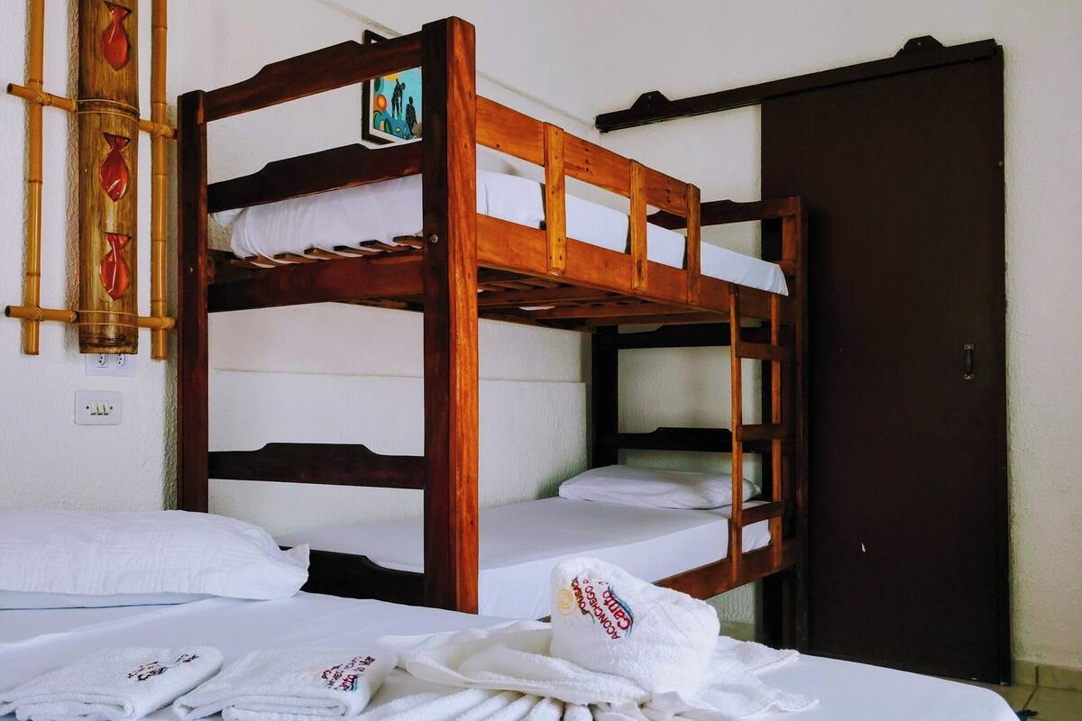 Quarto com beliche, roupa de cama branca, escada de madeira e uma porta.