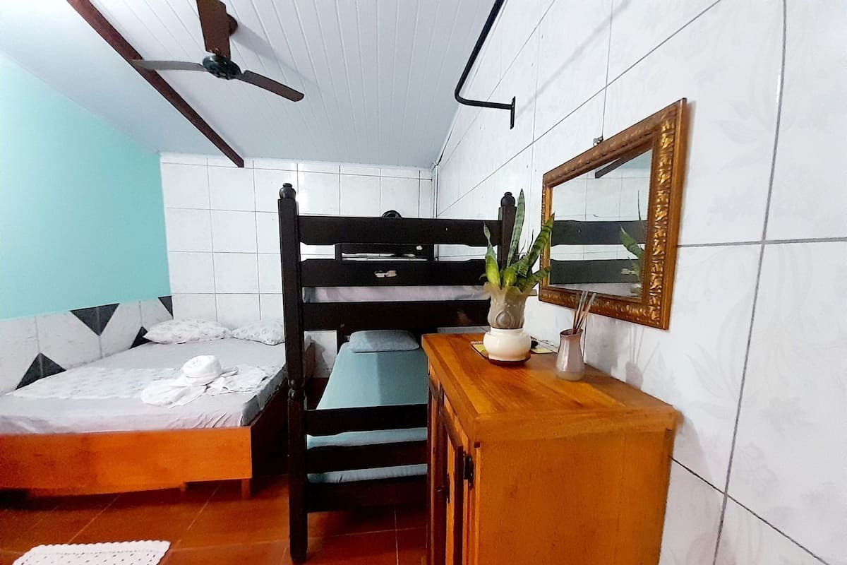 Um quarto com beliches, cômoda de madeira, espelho e ventilador de teto.