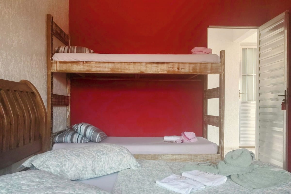 Quarto em dormitório com beliches, cabeceira de madeira e parede vermelha.