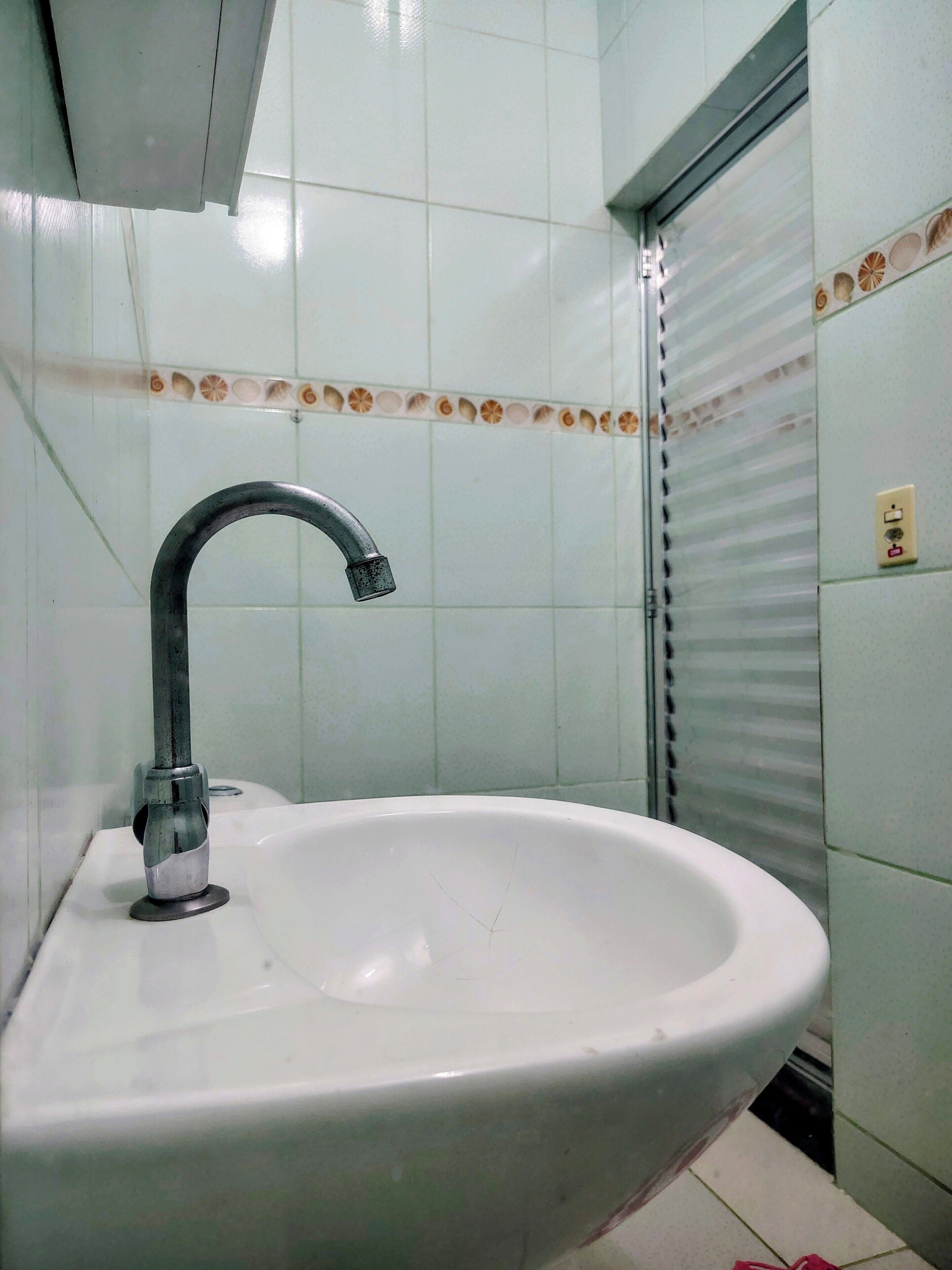 A bathroom with a white sink, a chrome faucet, and a tiled wall with a decorative border.