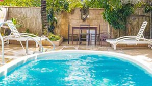 A swimming pool with clear blue water, surrounded by lounge chairs and a stone wall with greenery. - Pousada Aconchego Recanto Canto do Mar - São Sebastião - Caraguatatuba (São Sebastião)