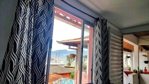A room with a window featuring a zebra-striped curtain, a view of a colorful mural outside, and a glimpse of a red-roofed building. - Pousada Aconchego Recanto Canto do Mar - São Sebastião - Caraguatatuba (São Sebastião)
