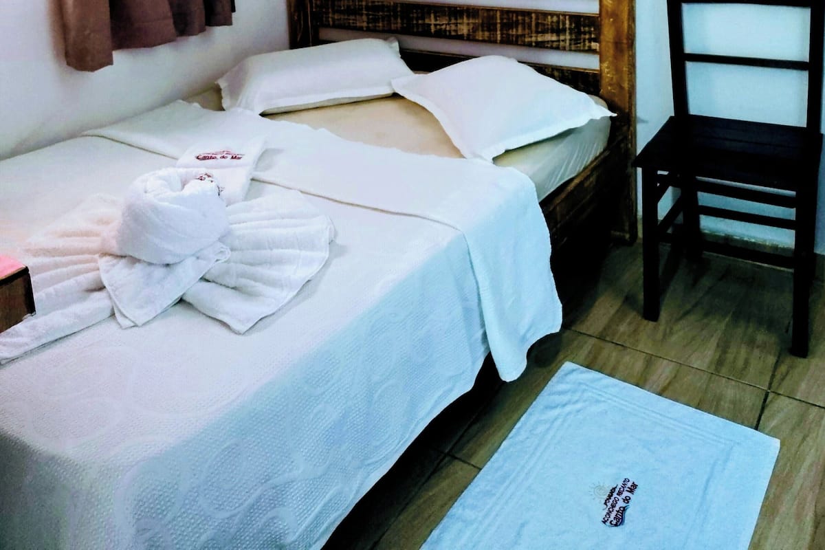 Uma cama de solteiro com lençóis brancos, cabeceira de madeira e um quadro na parede.