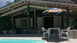 A pool area with a covered patio, outdoor seating, and a colorful umbrella. - Pousada Green House (Ubatuba)