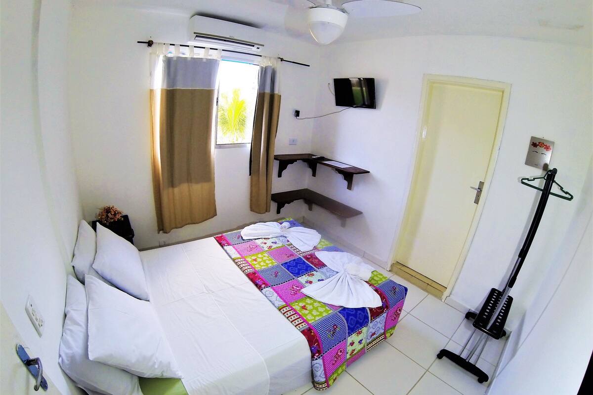 A bedroom with a bed, a TV, a ceiling fan, a window with curtains, a door, and a mop on the floor.