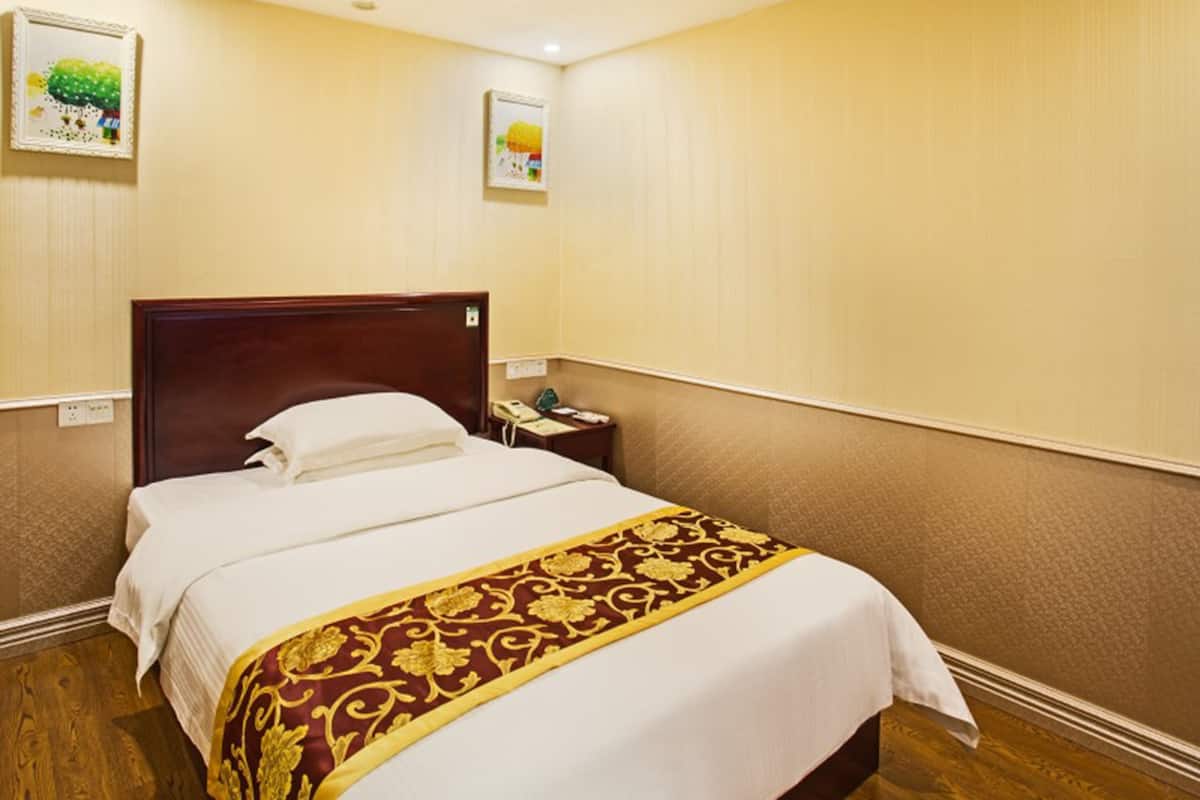 Quarto de hotel com cama de madeira, mesa de cabeceira com telefone e duas quadros na parede.