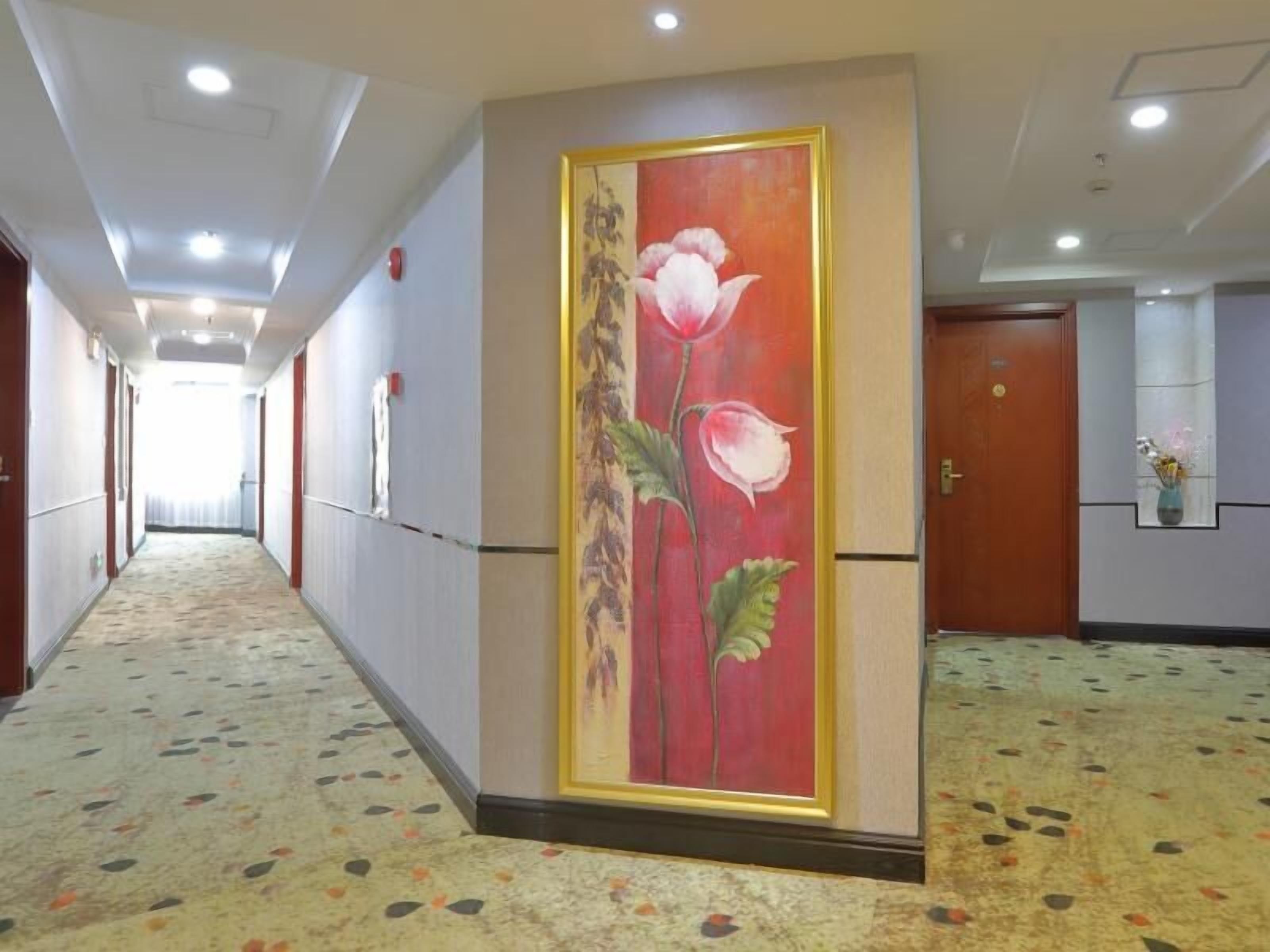 A hotel corridor with a floral mural on the wall, a patterned carpet, and a door at the end.