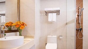 A bathroom with a white sink, toilet, and shower. There are flowers on the sink and a towel rack on the wall. - Vienna Hotel (Shenzhen Tianbao Road) (SHENZHEN)