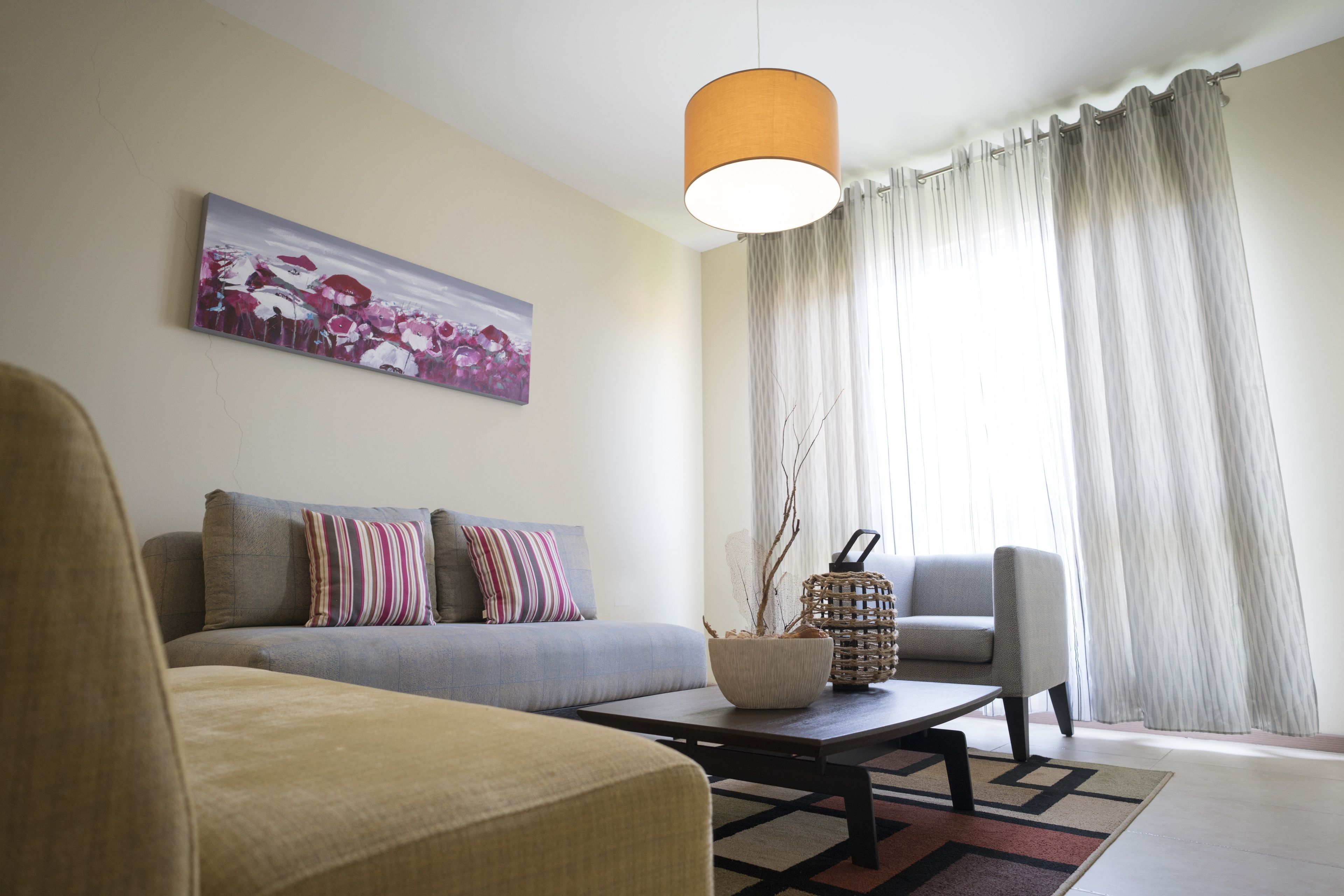 A living room with a sofa, armchair, coffee table, and a painting on the wall.