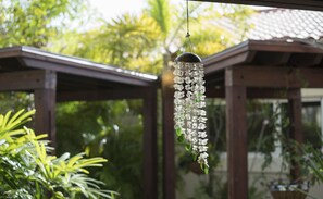 A hanging decorative item with white flowers and green leaves, suspended in a garden area with wooden structures and greenery in the background. - Costa Esmeralda Village (Noord)