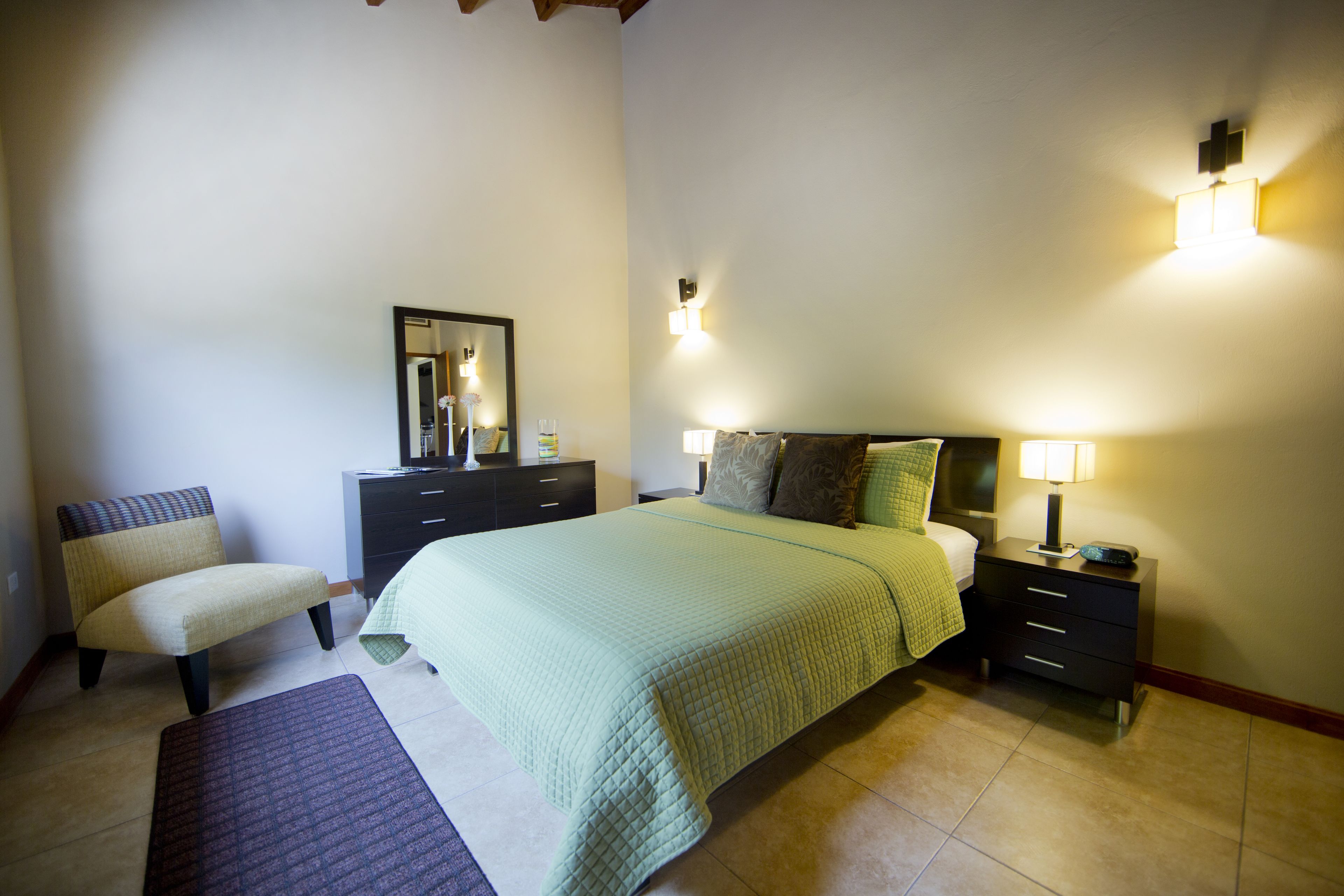 Une chambre à coucher comprenant un lit, des tables de chevet, une commode, une chaise et un miroir.