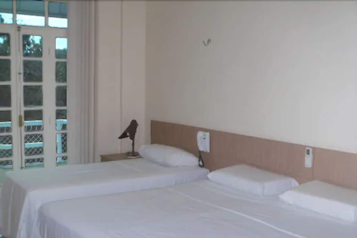Habitación de hotel con dos camas individuales, una mesita de noche, una lámpara y ventana con vistas al exterior.