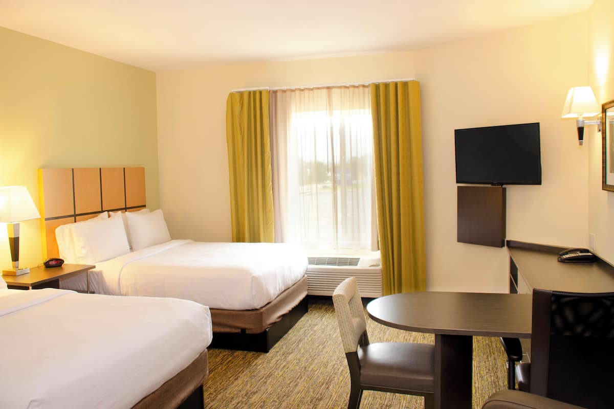 A hotel room with two beds, a desk with a chair, a television, and a window with curtains.
