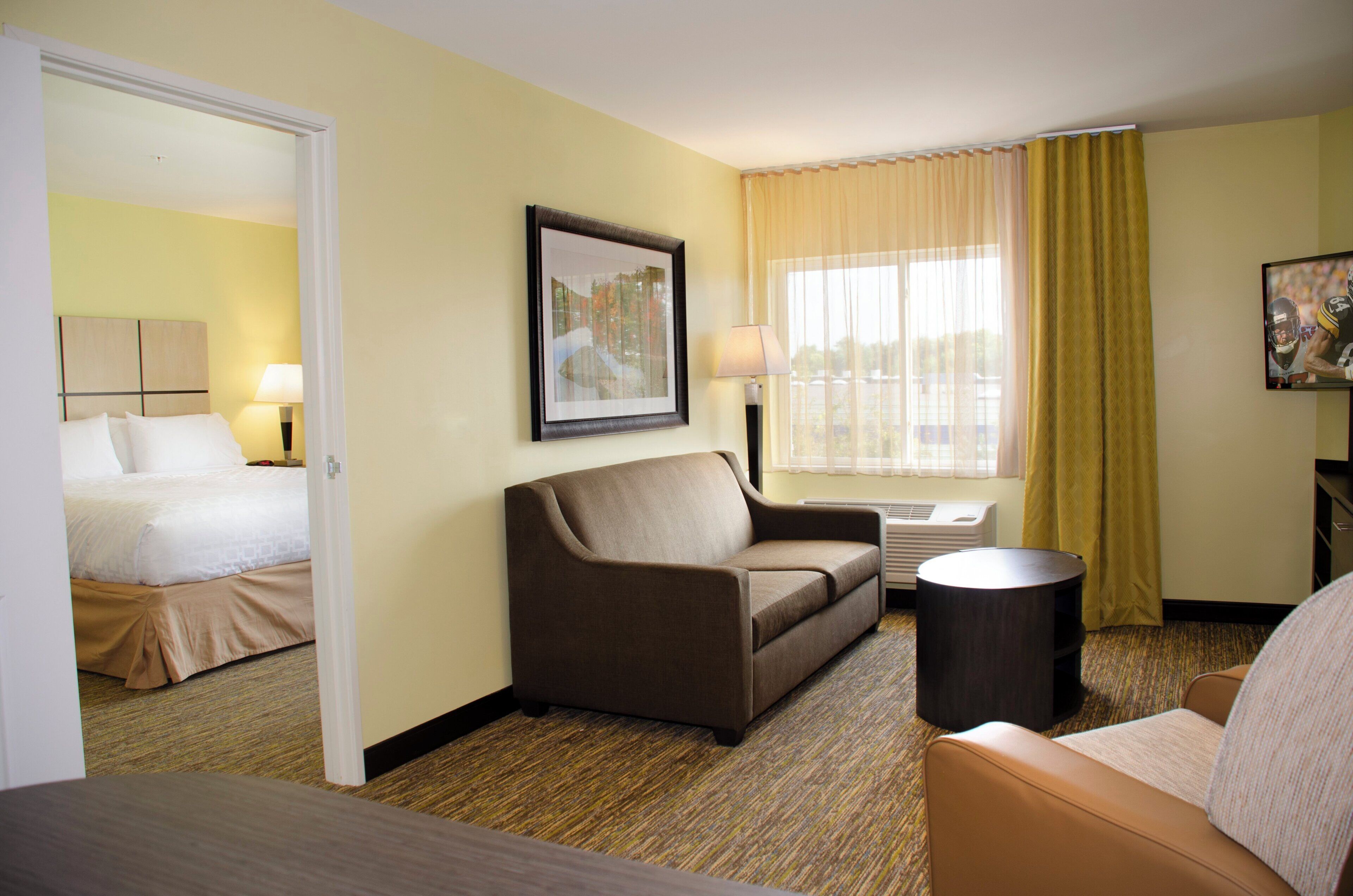 A hotel room with a bed, a sofa, a small table, a lamp, a picture on the wall, and a window with curtains.