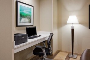 Habitación de hotel con escritorio, impresora, ordenador portátil, silla, lámpara de pie y un cuadro en la pared.