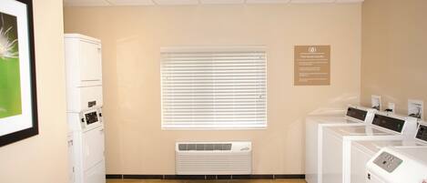 A laundry facility with multiple washing machines, a vent, and a sign indicating free guest laundry.