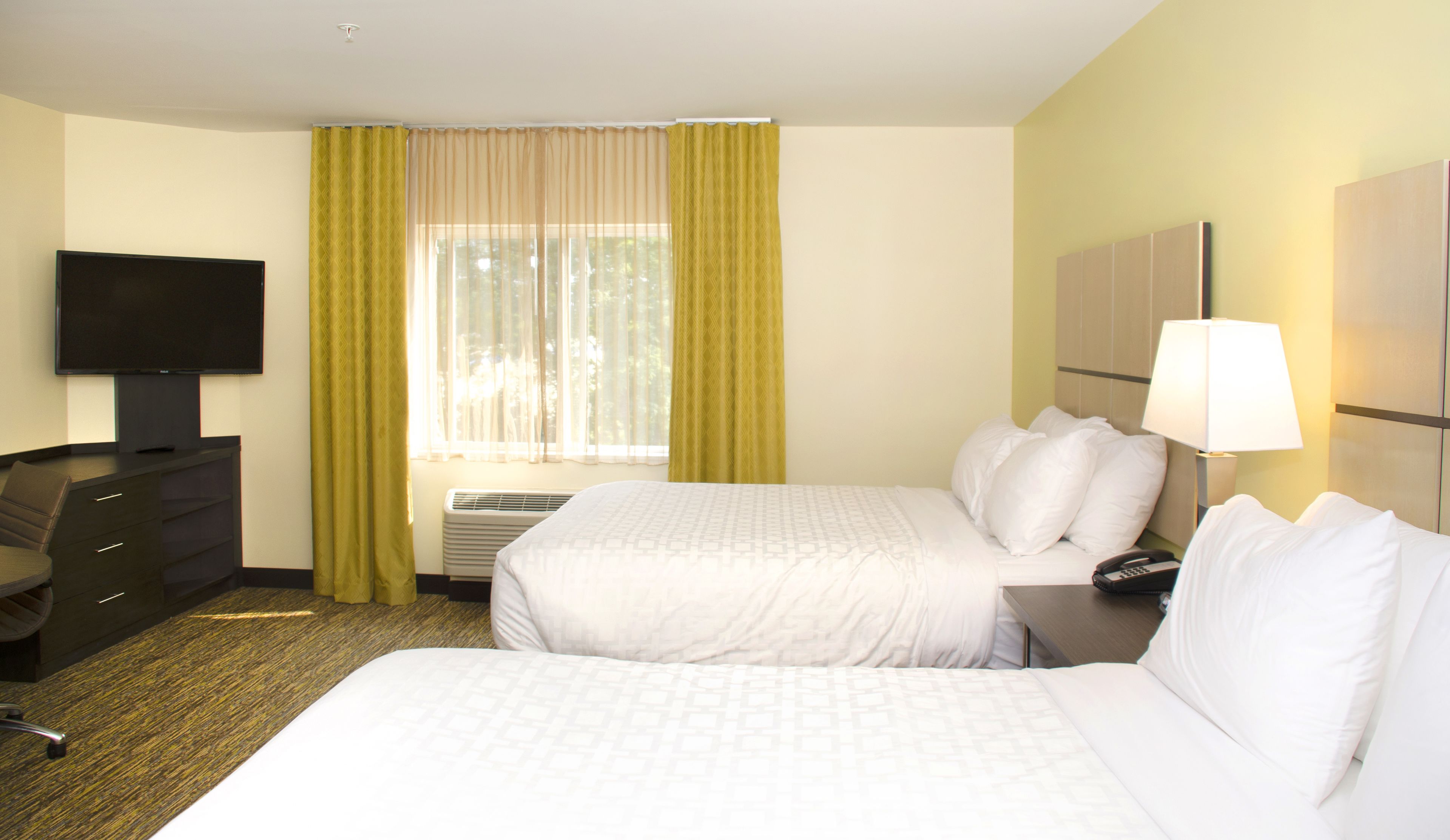 Una habitación de hotel con dos camas, un escritorio con silla, televisión y ventana con cortinas.