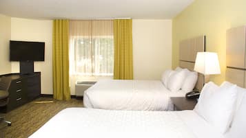 Una habitación de hotel con dos camas, un escritorio con silla, televisión y ventana con cortinas.