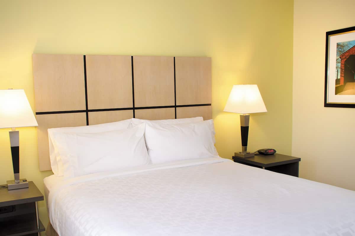 A neatly made bed with white linens, two bedside lamps, and a nightstand with a clock.