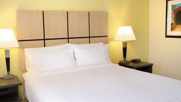 Uma cama bem arrumada com lençóis brancos, duas luminárias de cabeceira e uma mesa de cabeceira com um relógio.