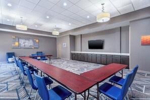 Un salón de conferencias con una mesa larga, sillas azules, un televisor de pantalla plana y una alfombra estampada.