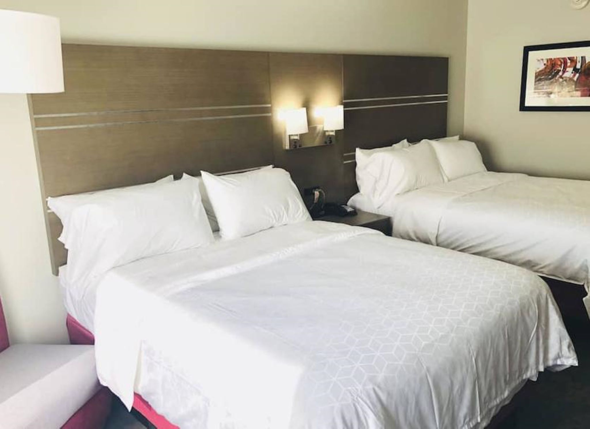 Habitación de hotel con dos camas, cada una con ropa de cama blanca y cabeceros. Hay dos lámparas fijadas a los cabeceros.