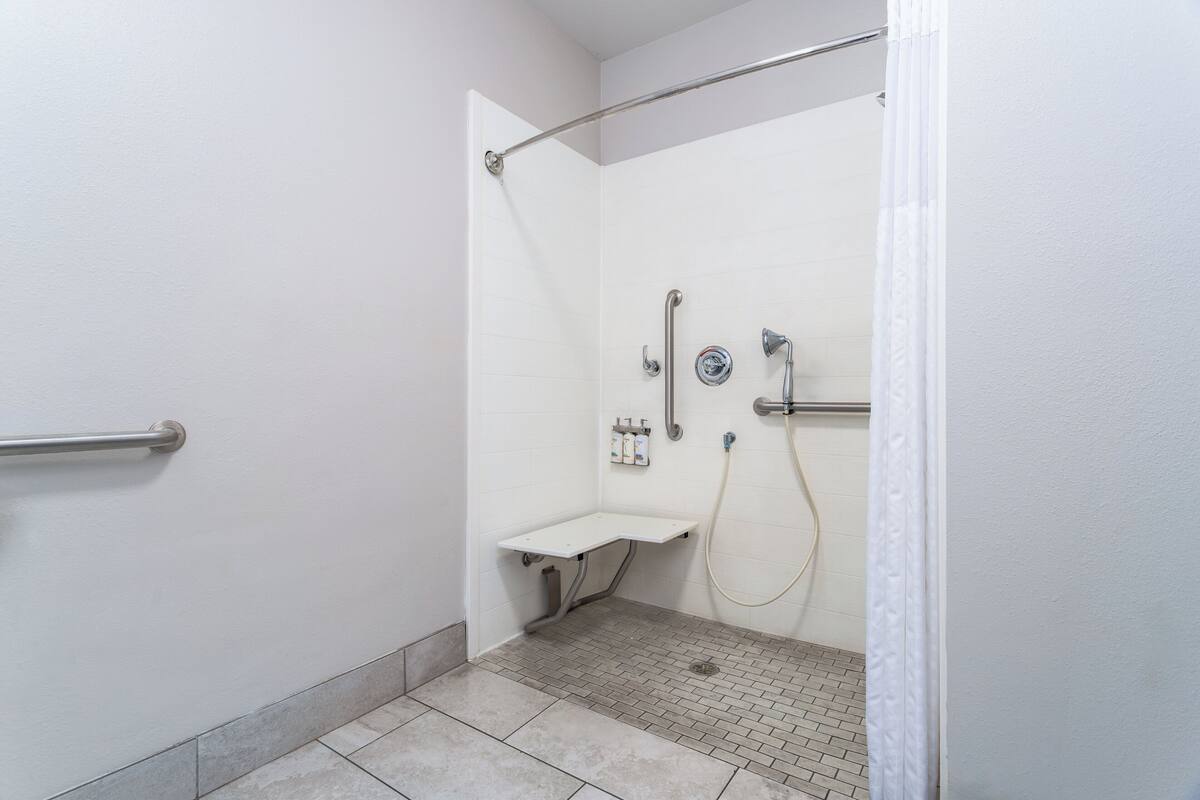 A shower area with a grab bar, a handheld showerhead, and a handheld faucet.