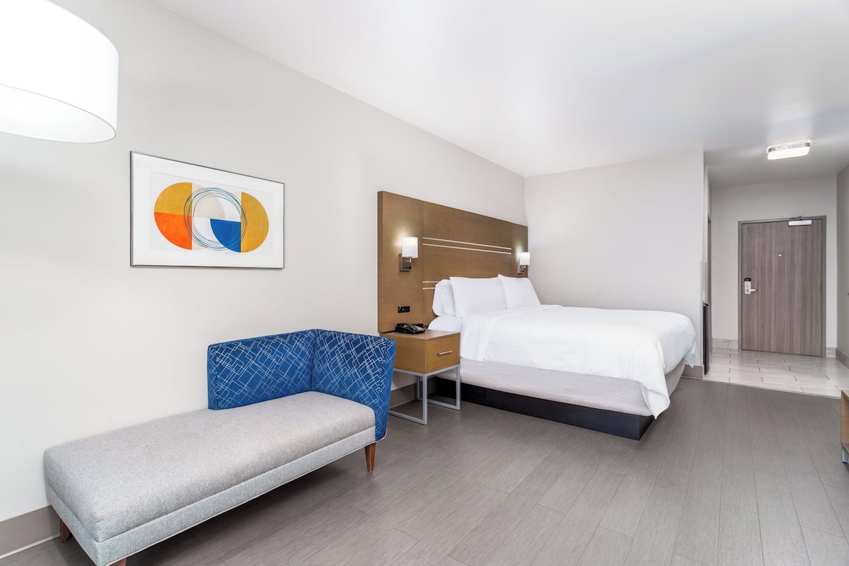A modern hotel room with a bed, a bench, a desk, and a wall-mounted artwork.