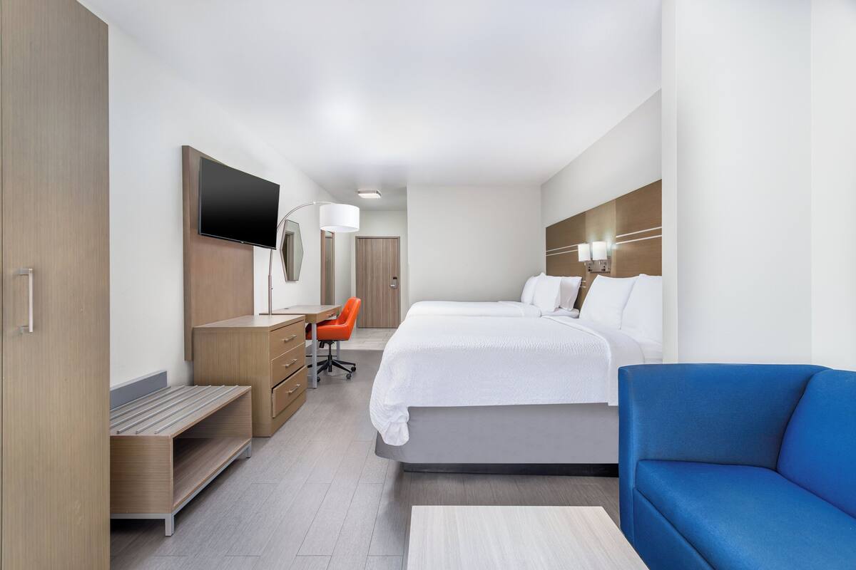 A modern hotel room with a bed, a desk, a chair, a TV, and a sofa.