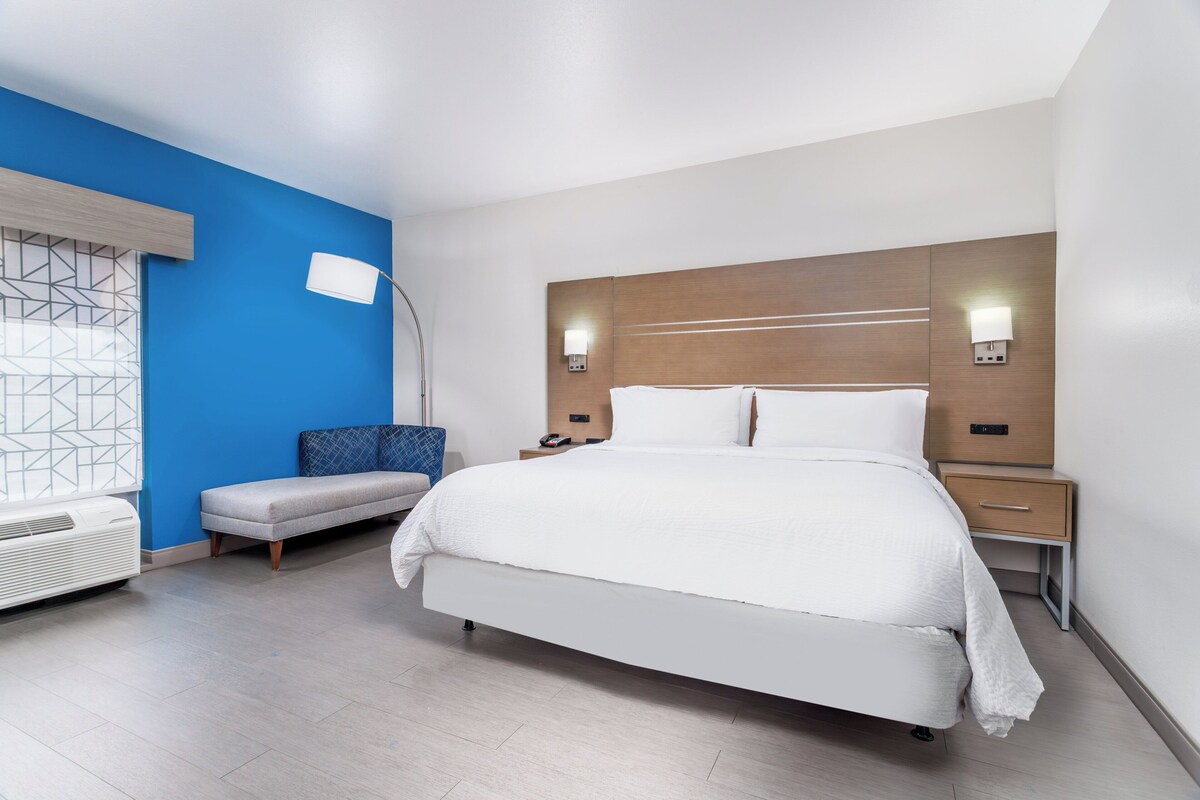 Una habitación de hotel moderna con una cama grande, una mesita de noche, una lámpara y una pared de acento azul.