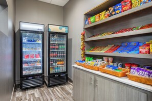Dos dispensadores refrigerados para bebidas, una estantería con productos de snack y un mostrador con cestas de aperitivos.