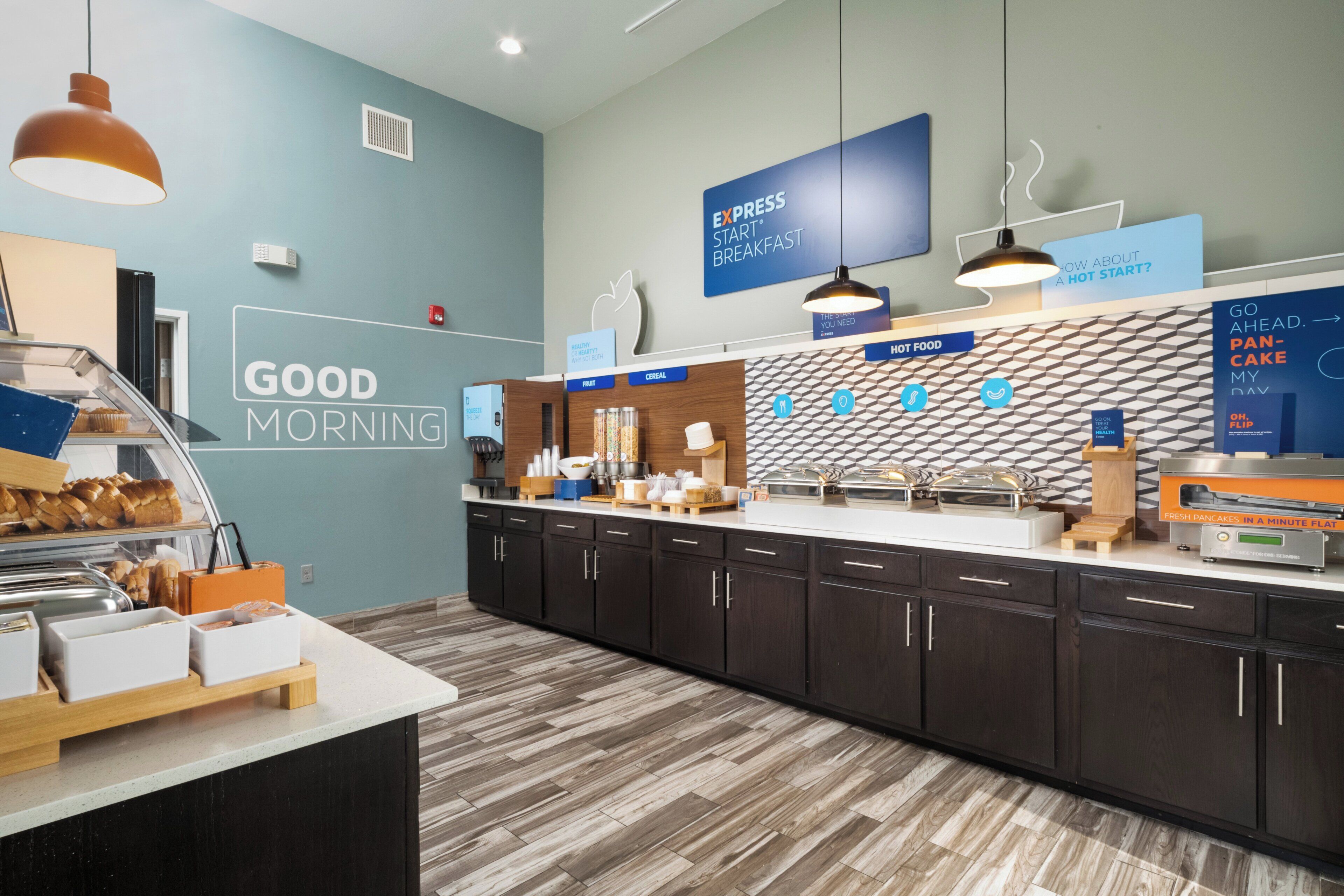 Een ontbijtruimte met een toonbank waarop diverse etenswaren staan, een muur met een 'Good Morning' bord en verlichting.