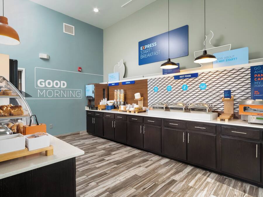 Een ontbijtruimte met een toonbank waarop diverse etenswaren staan, een muur met een 'Good Morning' bord en verlichting.