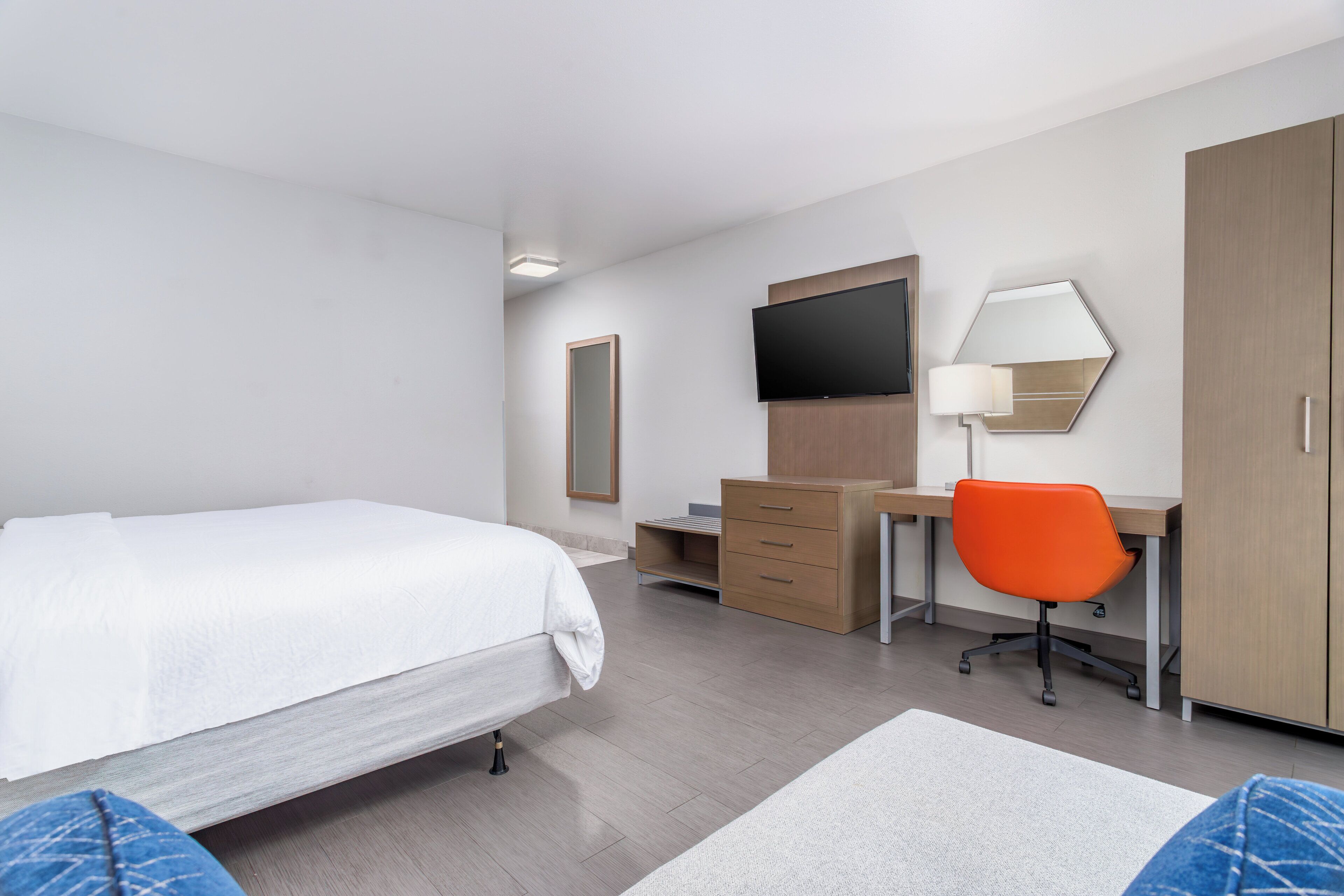 Moderni hotellihuone, jossa on sänky, työpöytä, tuoli, vaatekaappi ja litteänäyttöinen televisio.