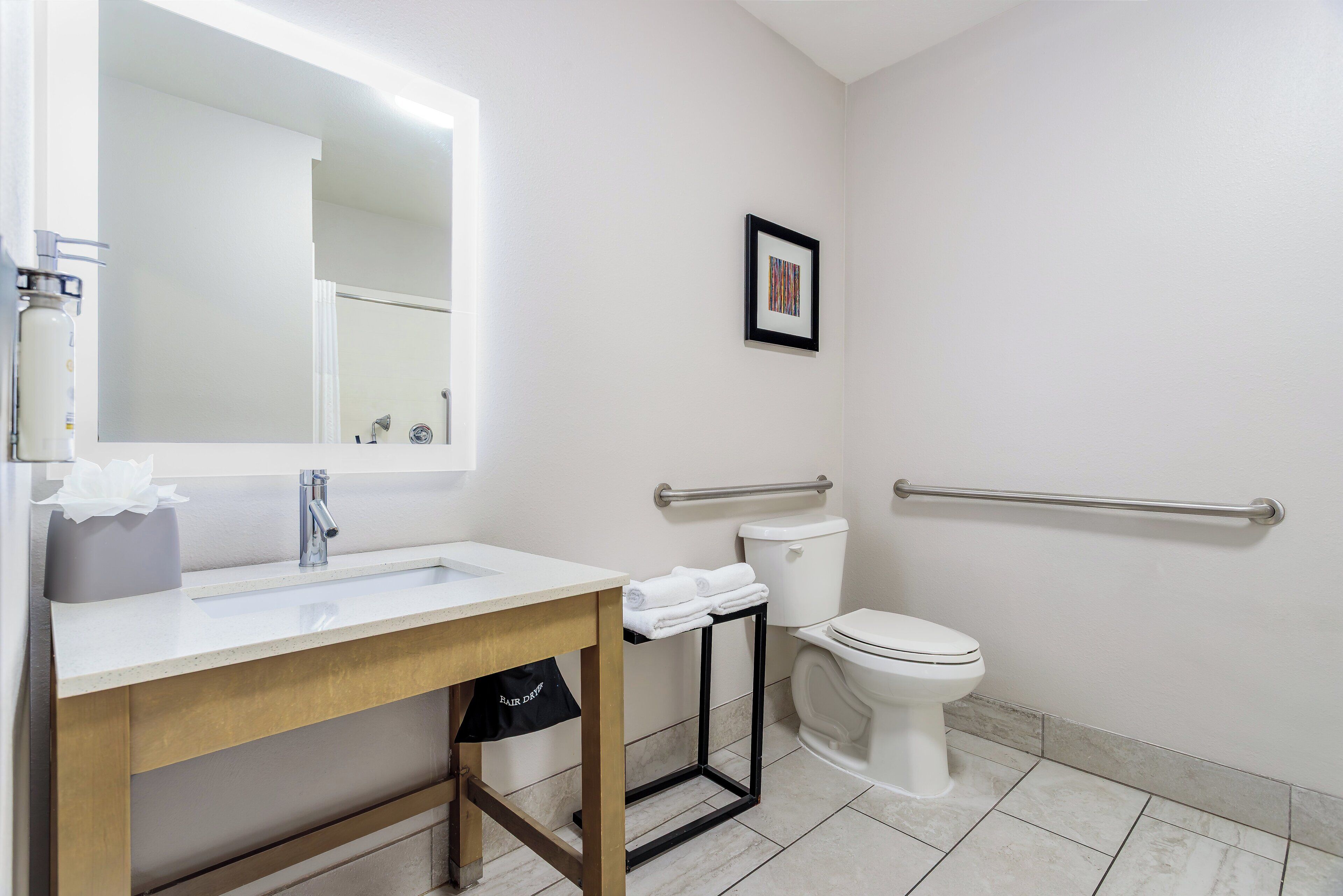 A bathroom with a sink, mirror, toilet, and handrails.
