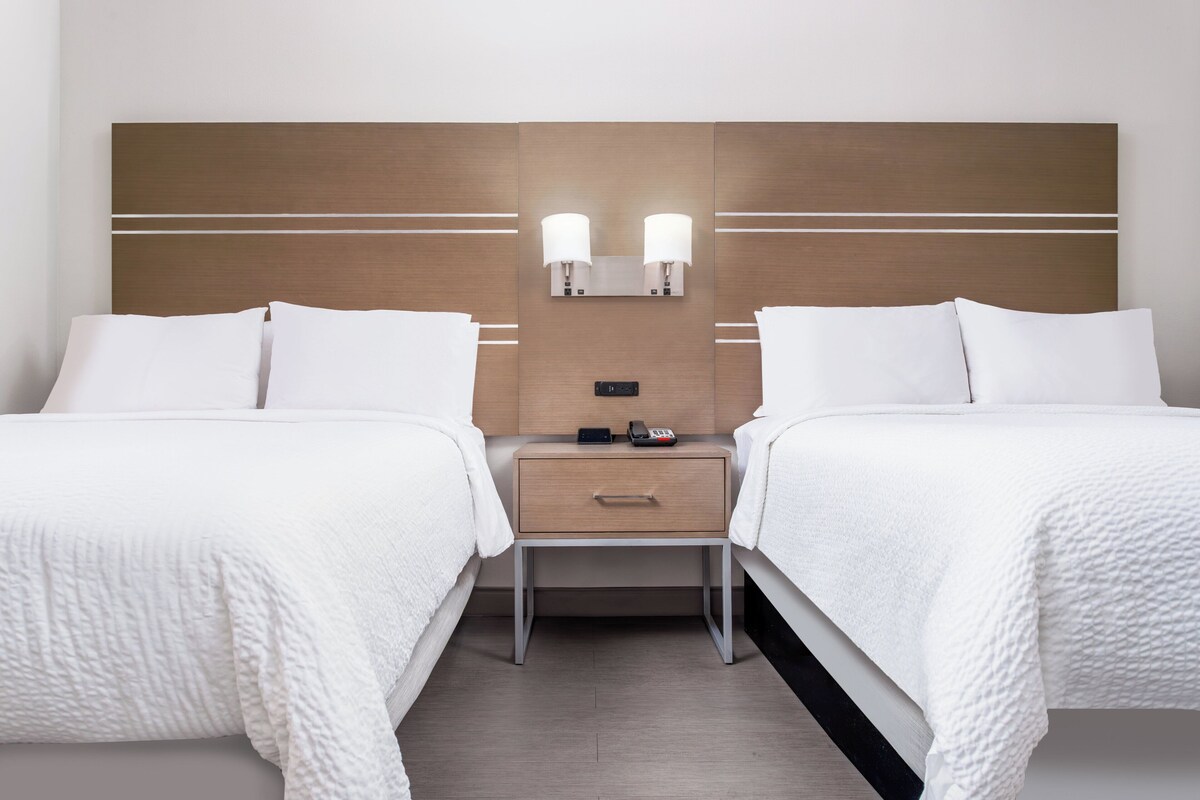 Una habitación de hotel con dos camas, una mesita de noche con lámpara y un panel de control.