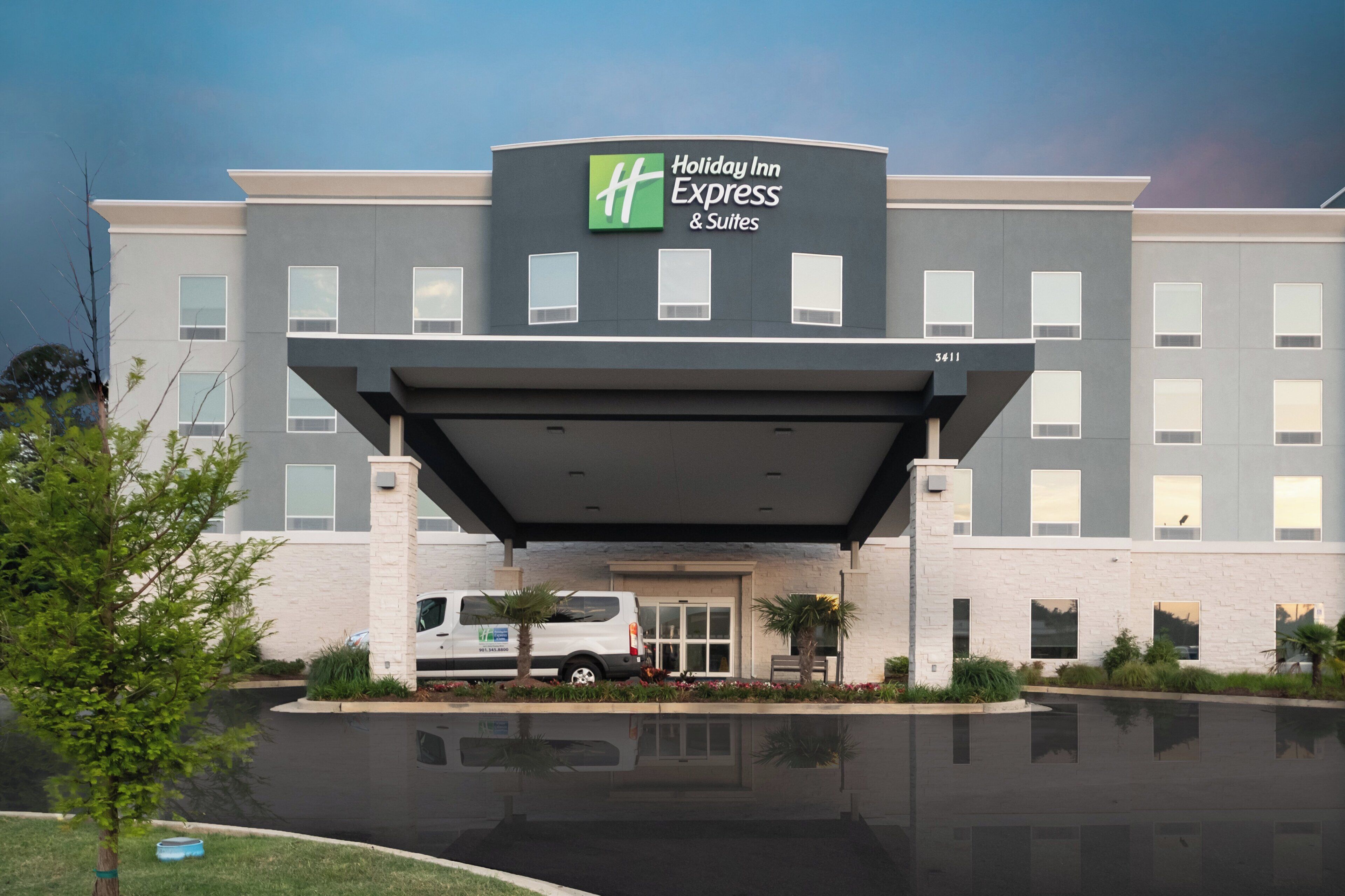 Edificio de Holiday Inn Express & Suites con entrada cubierta, zona de estacionamiento y piscina reflectante.