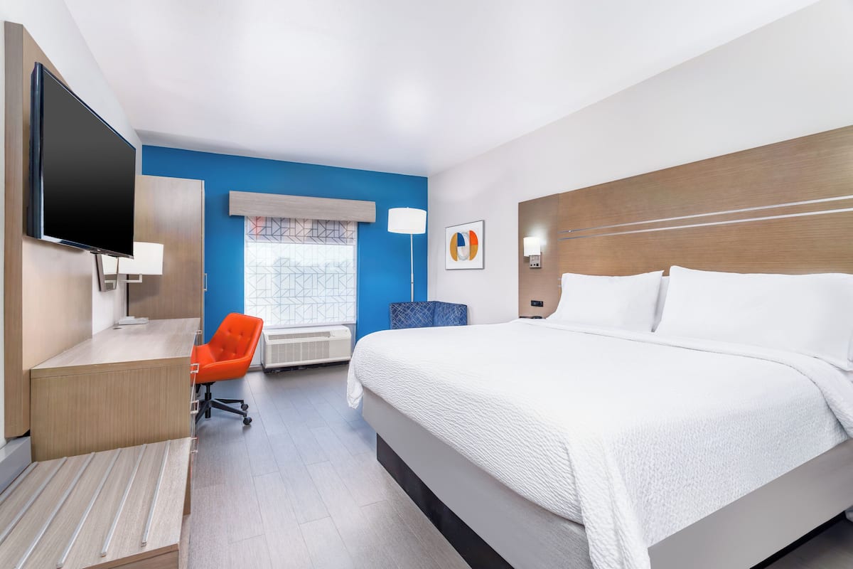 A hotel room with a bed, a desk, a chair, a TV, and a window with a view.