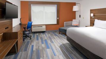 A hotel room with a bed, a desk, a chair, a TV, a window, and a heater.